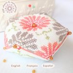 Patrón de punto de cruz para Aster biscornú, bordado con margaritas en colores coral y gris con detalles en verde.