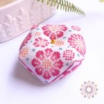 Octagonal embroidered biscornu pin cushion with geometrical Gerbera flowers in warm hues of pink. Embroidered in cross and diamond stitches.